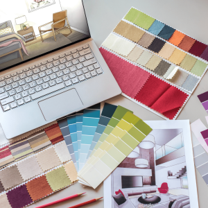 A workspace with fabric swatches and color palettes arranged near a laptop and architectural drawings. The fabric samples display a variety of colors, from neutral shades to vibrant tones. The setup suggests a focus on interior design, color coordination, and material selection, typical of the creative process in interior design projects in Paarl.