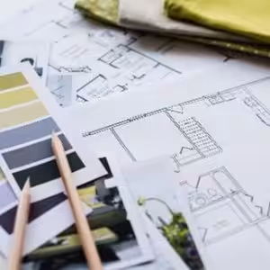 An interior design workspace featuring architectural blueprints, fabric samples, and color swatches. The plans detail a home layout, and the fabric choices include vibrant green tones. A pencil rests on a photo of a completed room, highlighting the design process from concept to final execution, typical of interior designers' projects in Paarl.